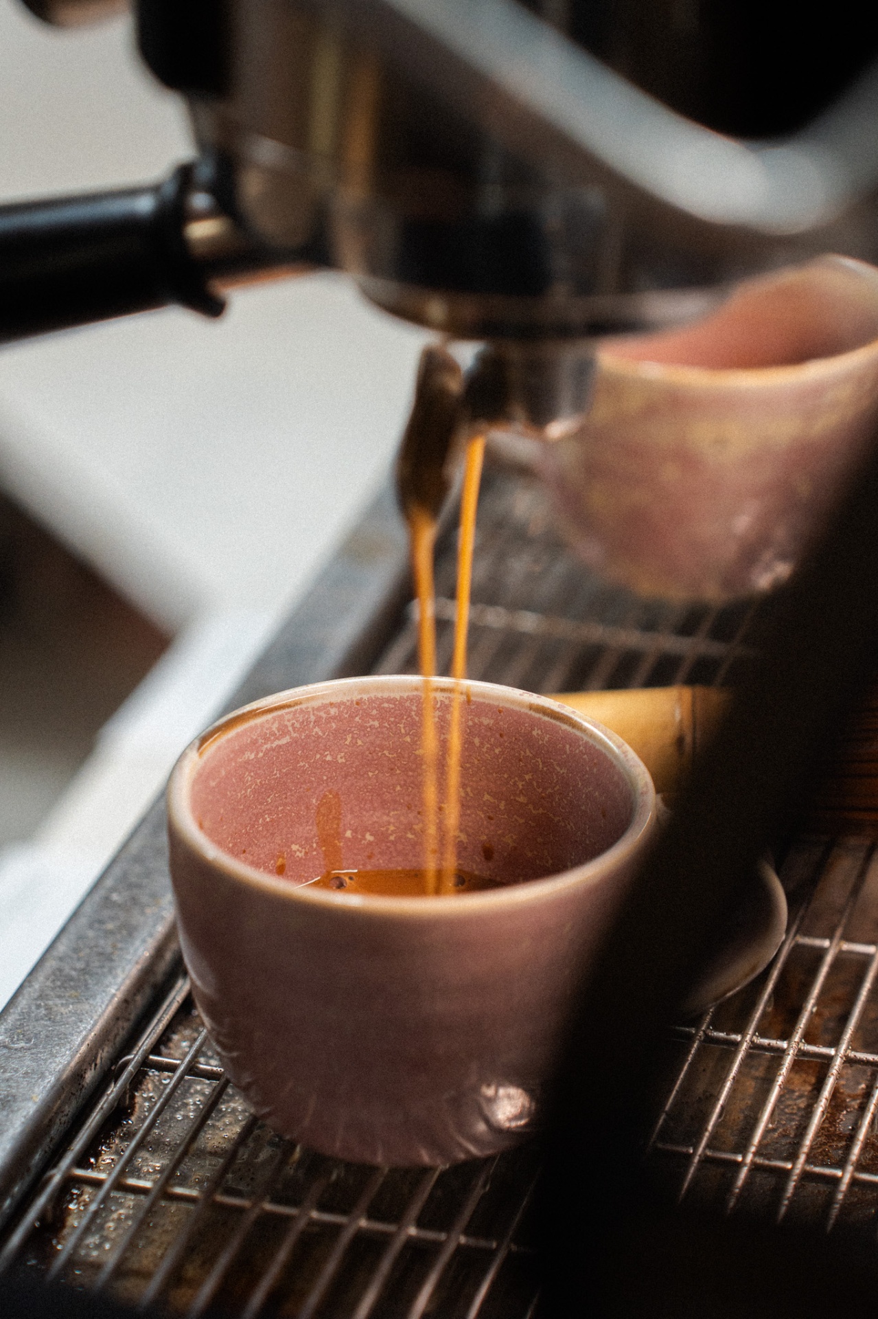 Espresso pouring into a pink ceramic cup on an espresso machine drip tray
