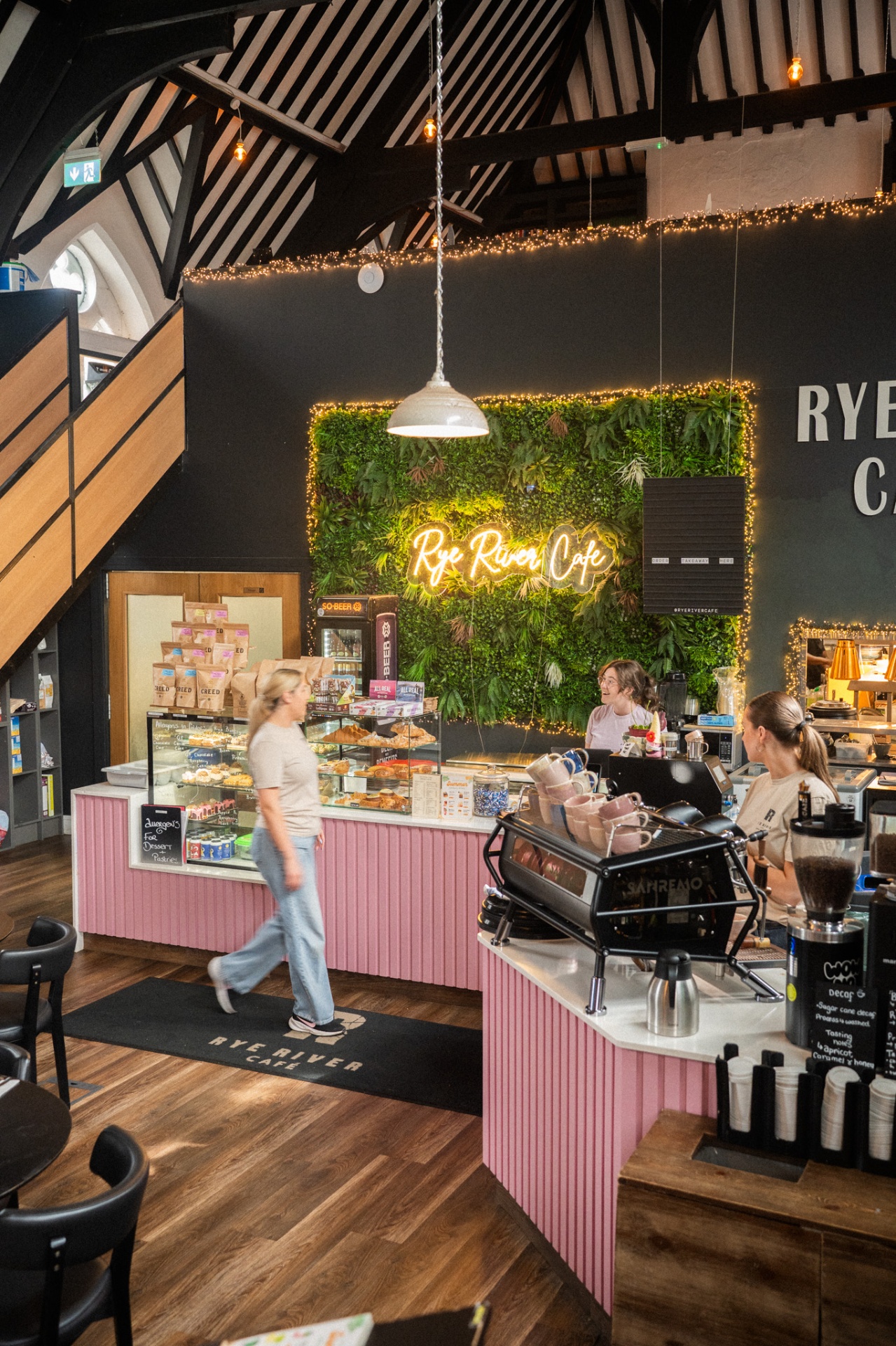Interior of Rye River Cafe in Kilcock with neon sign, living plant wall, pink counter and barista at the espresso machine